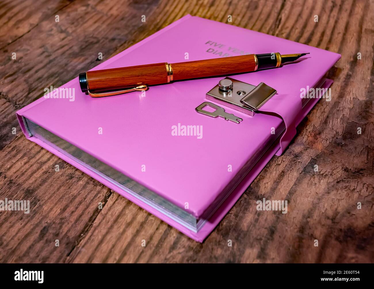 Un journal intime verrouillable rose de cinq ans et un stylo fontaine en bois sur fond en bois Banque D'Images