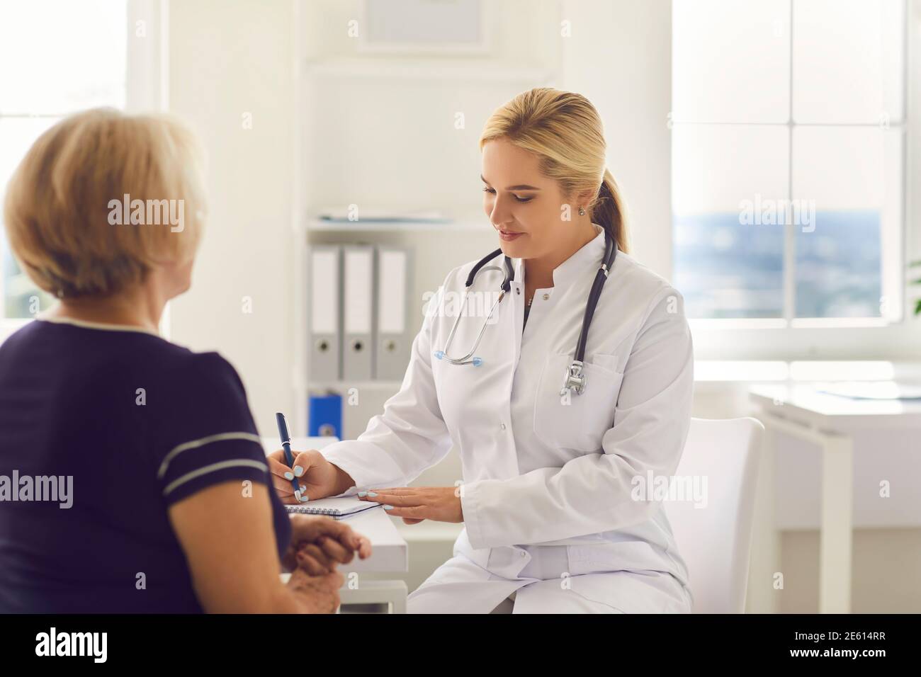 Jeune femme souriante médecin écrivant des plaintes de femme âgée patient Banque D'Images