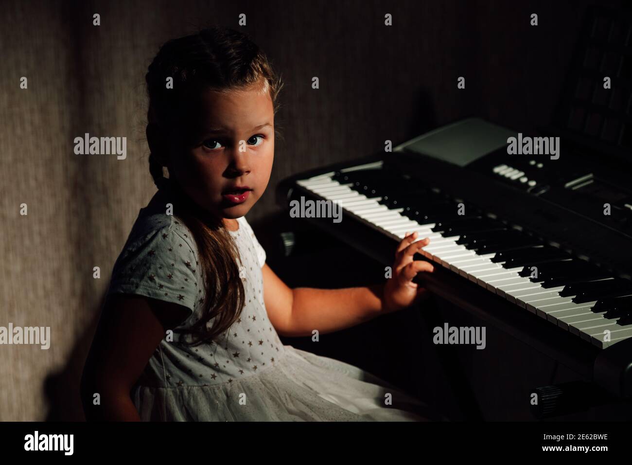 portrait dans une clé basse d'une fille effrayée jouant un synthétiseur électronique la nuit dans un intérieur de maison Banque D'Images