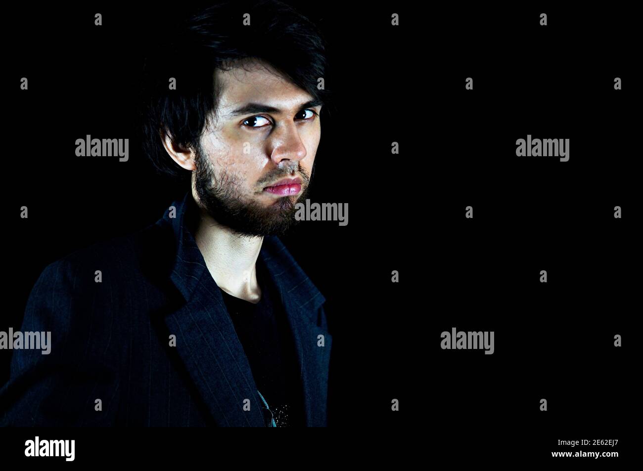 Homme regardant la caméra avec une expression sérieuse, portant un costume sur un fond noir Banque D'Images