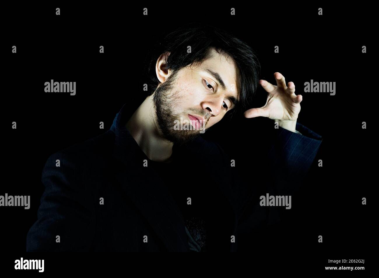 Jeune homme regardant vers le bas avec sa main gauche vers le haut faisant une pose, avec sa tête et la main étant lumineuse Banque D'Images