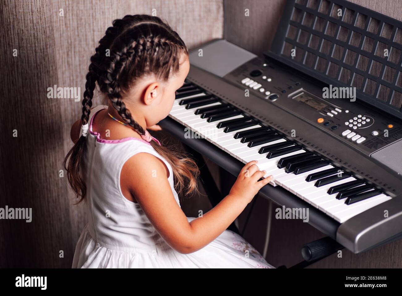 vue latérale d'une fille dans une robe blanche d'été et deux queues de cochon jouent un synthétiseur électronique dans un intérieur de maison Banque D'Images