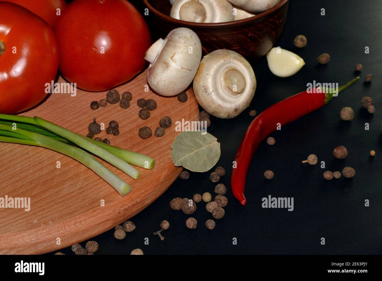 Gros plan sur les champignons frais, le piment rouge, la tomate, l'ail, la feuille de Laurier et les épices. Arrière-plan sombre Banque D'Images