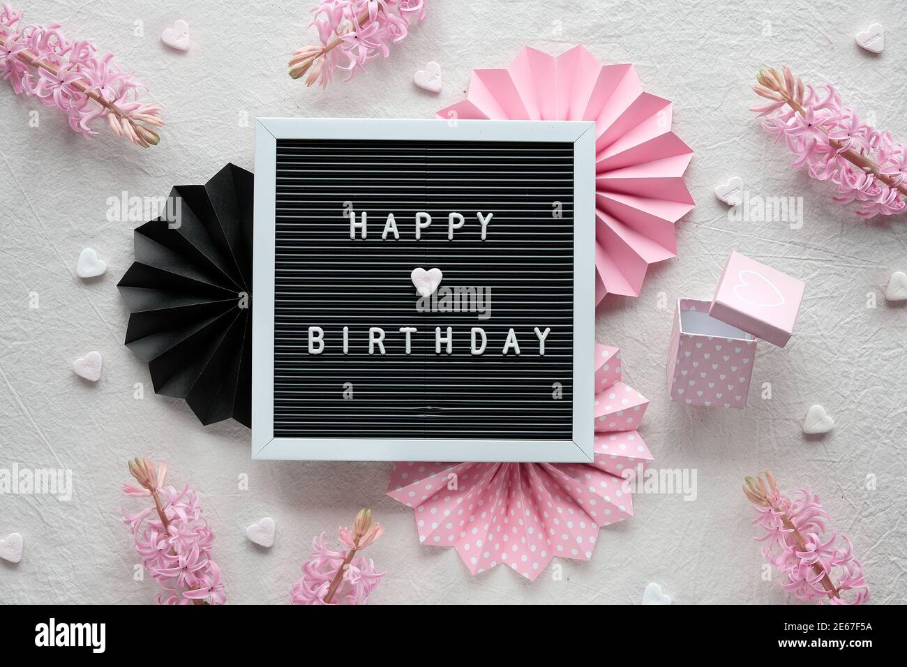 Texte Joyeux anniversaire sur le tableau de texte, le tableau de lettres. Tissu blanc crème, plat et original, rose et noir. Décoration de fête, ventilateurs en papier, coeurs et cadeaux Banque D'Images