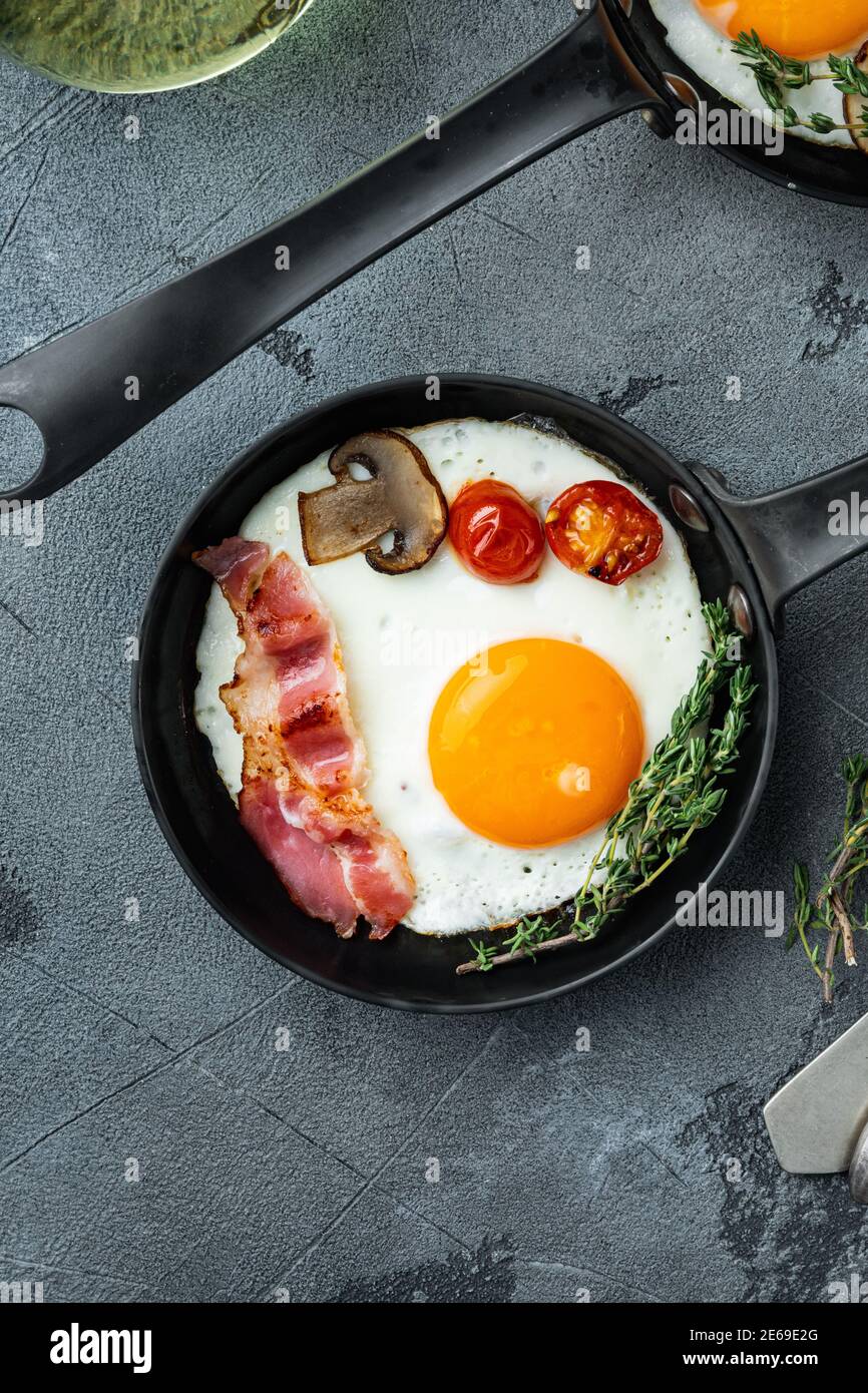 Œufs frits avec bacon et légumes dans une poêle en fonte, sur fond gris, vue de dessus plat Banque D'Images