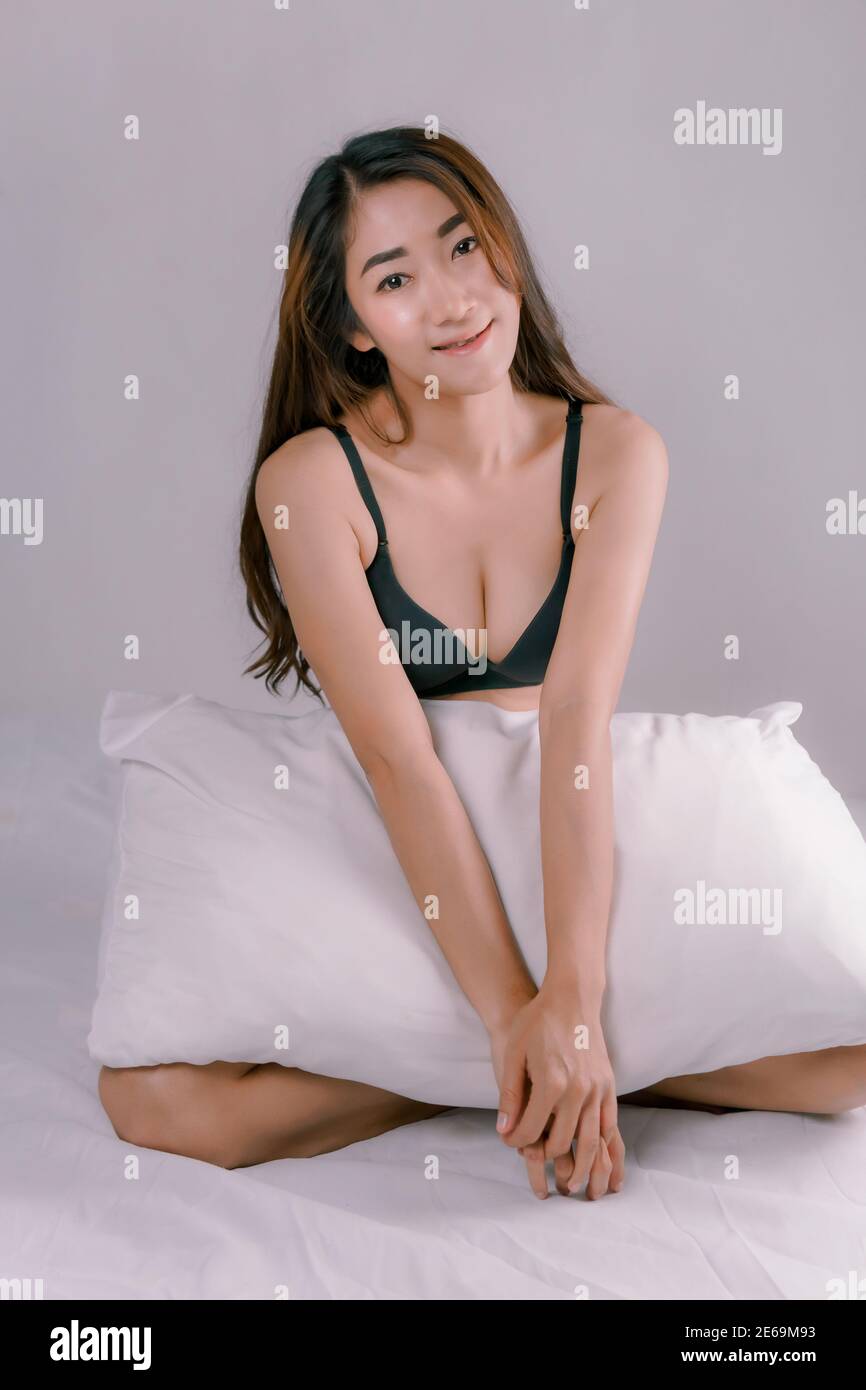Une femme asiatique sexy portant un bikini noir est assise sur le lit blanc. Banque D'Images