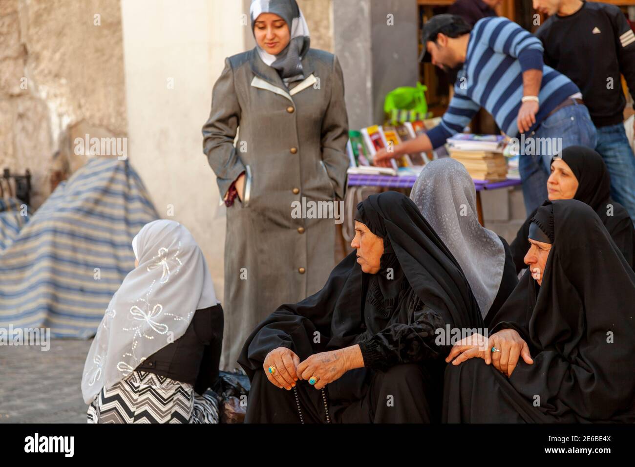 Damas, Syrie 03-28-2010: Un groupe de femmes musulmanes âgées portant des burqas noirs sont assis sur le trottoir près du bazar. Autres femmes avec coloré Banque D'Images