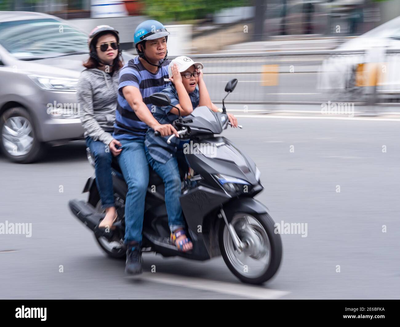 Moto avec trois personnes à la vitesse dans le District 1, Ho Chi Minh ville, Vietnam. La photo, à l'exception du conducteur, est floue en raison de la vitesse. Banque D'Images