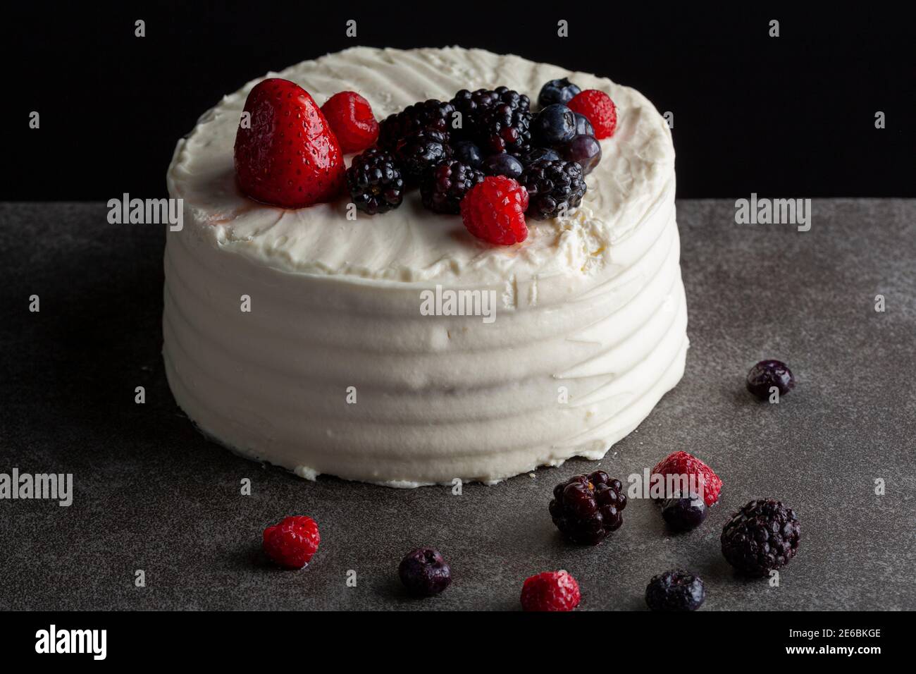 Gros plan sur l'image d'un gâteau rond avec glaçage blanc crémeux et assortiment de baies utilisées comme garnitures décoratives. Servi sur un baba noir gris foncé Banque D'Images