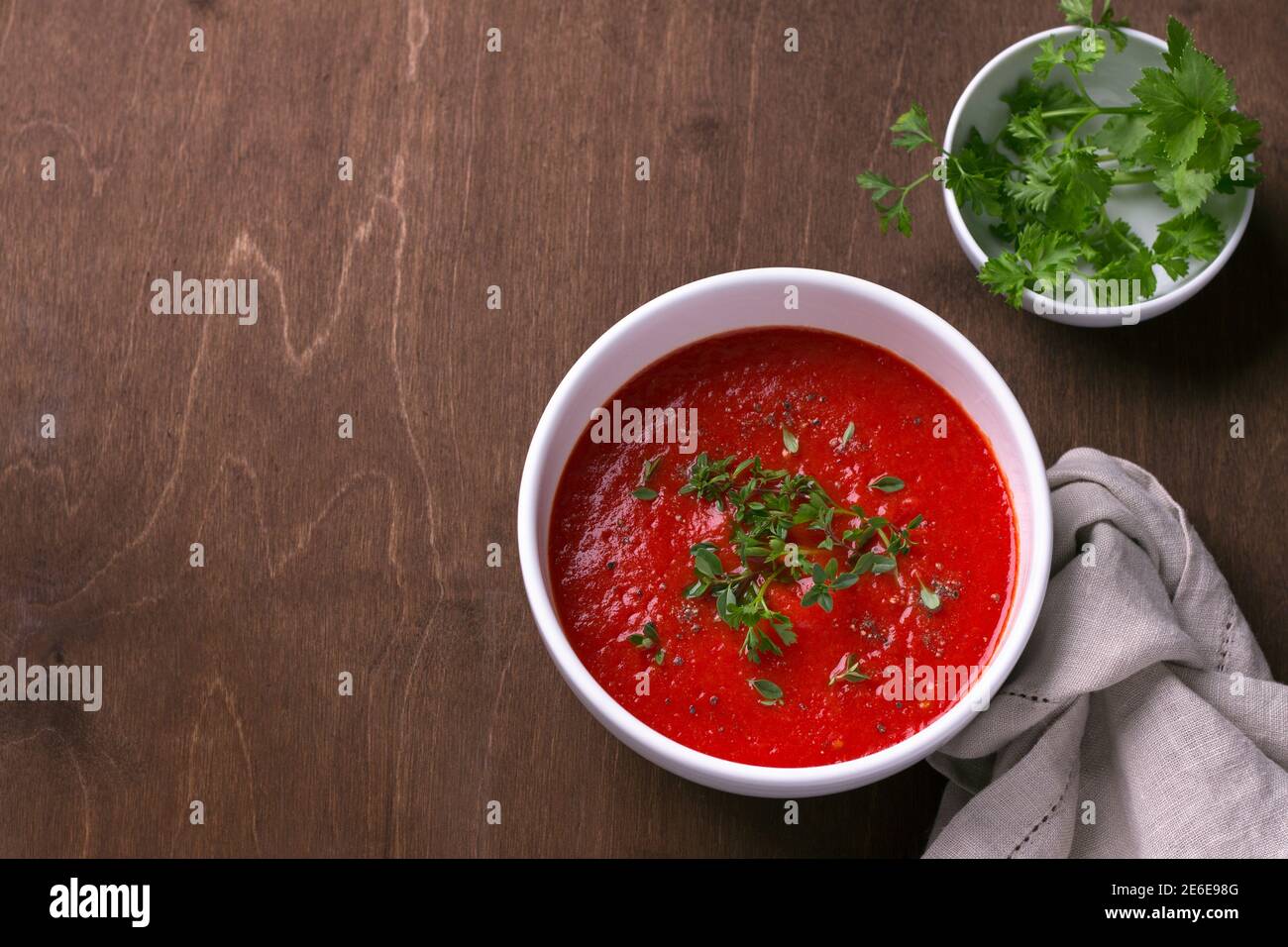 Délicieuse soupe végétalienne de tomates cuites au four et de poivrons avec des herbes dans une assiette blanche sur un fond en bois, vue de dessus, espace libre, horizontale Banque D'Images