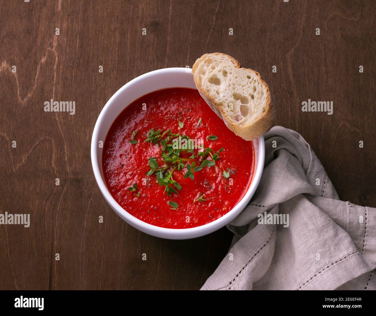 Délicieuse soupe végétalienne de tomates cuites au four et de poivrons avec herbes dans une assiette blanche sur un fond de bois, vue du dessus Banque D'Images