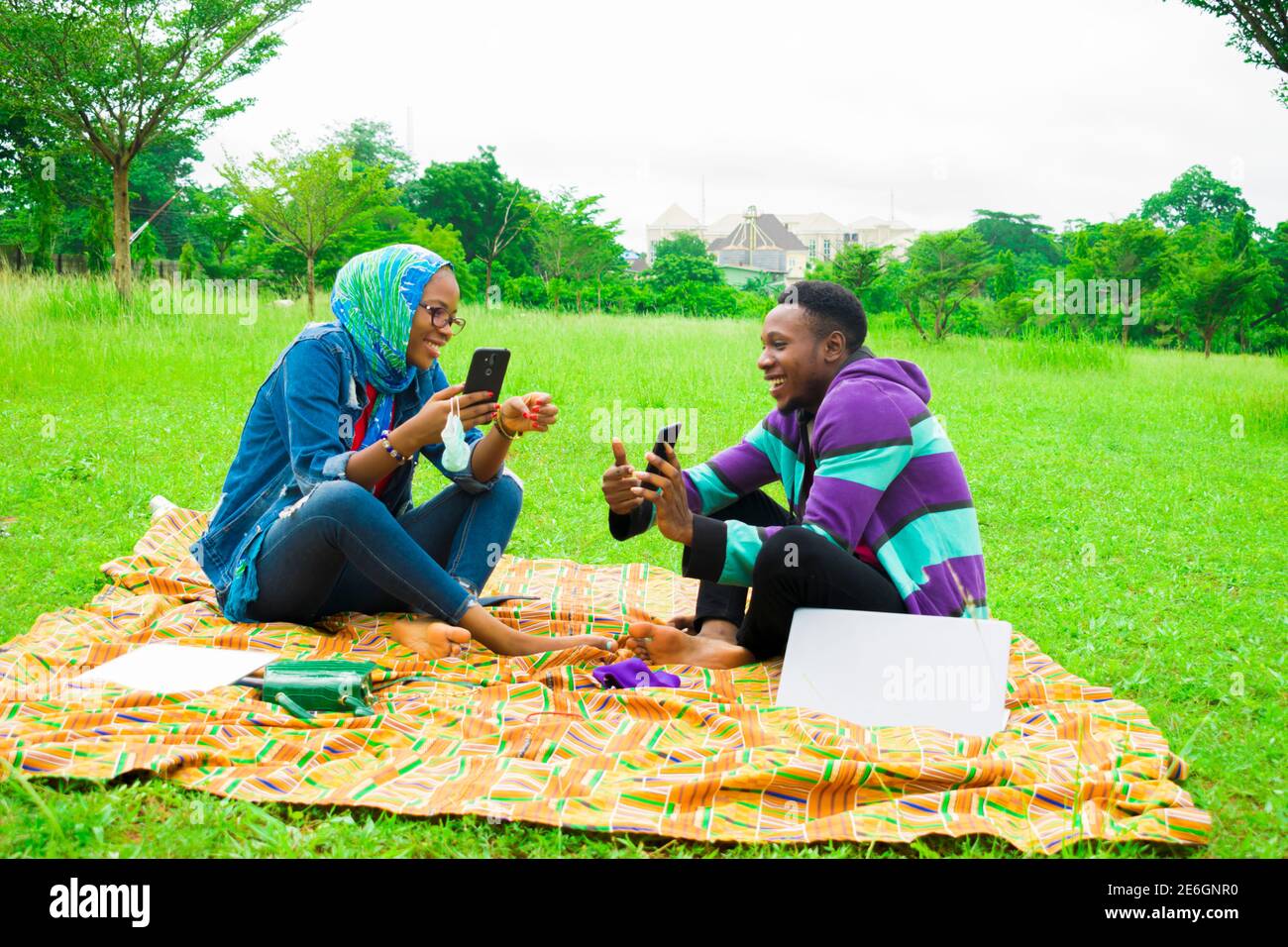 jeunes couples noirs assis dans un parc, utilisant leur smartphone pour surfer sur internet Banque D'Images