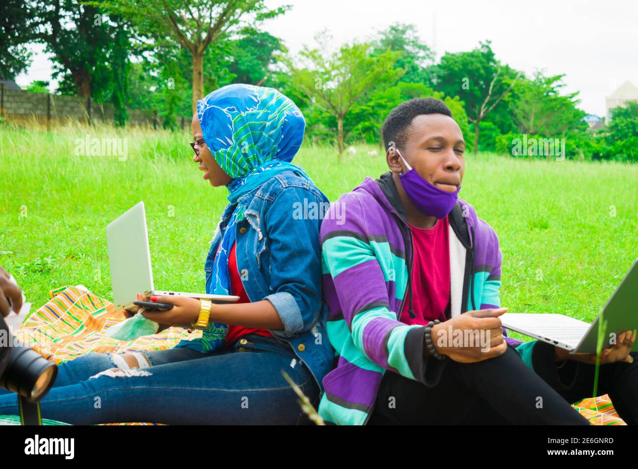 jeunes couples noirs assis dans un parc, utilisant leurs ordinateurs portables pour surfer sur internet Banque D'Images