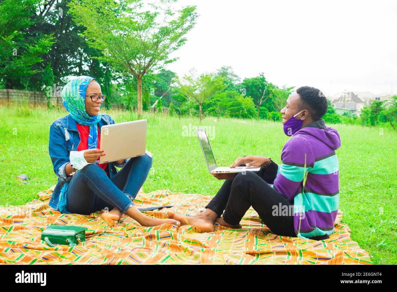 jeunes couples noirs assis dans un parc, utilisant leurs ordinateurs portables pour surfer sur internet Banque D'Images