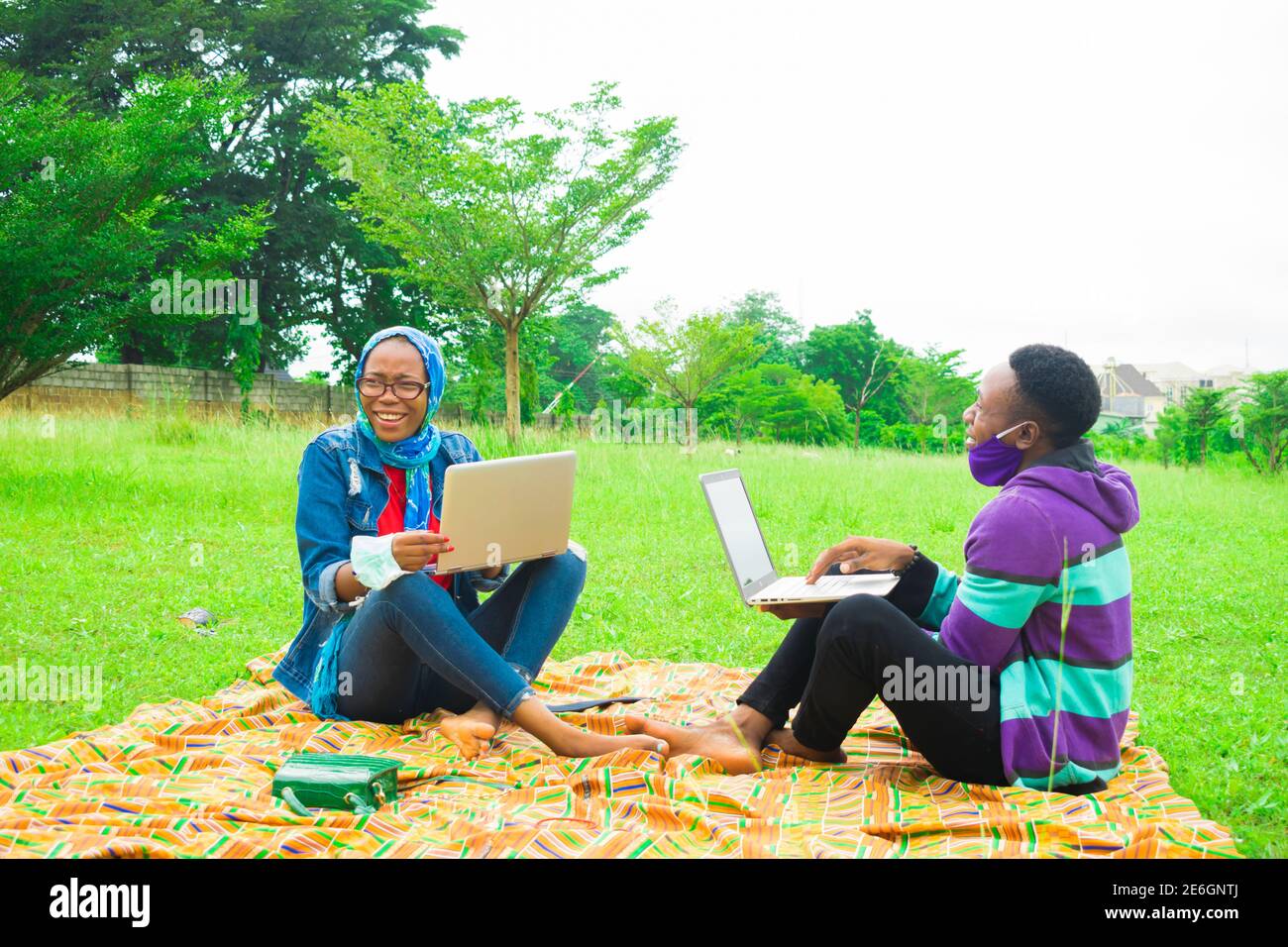 jeunes couples noirs assis dans un parc, utilisant leurs ordinateurs portables pour surfer sur internet Banque D'Images