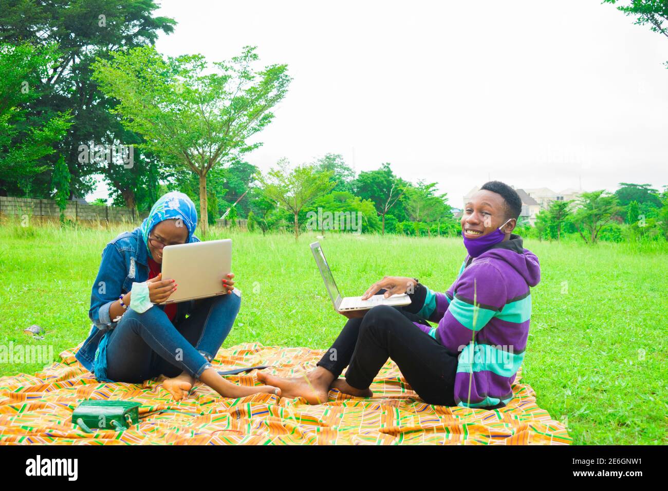 jeunes couples noirs assis dans un parc, utilisant leurs ordinateurs portables pour surfer sur internet Banque D'Images