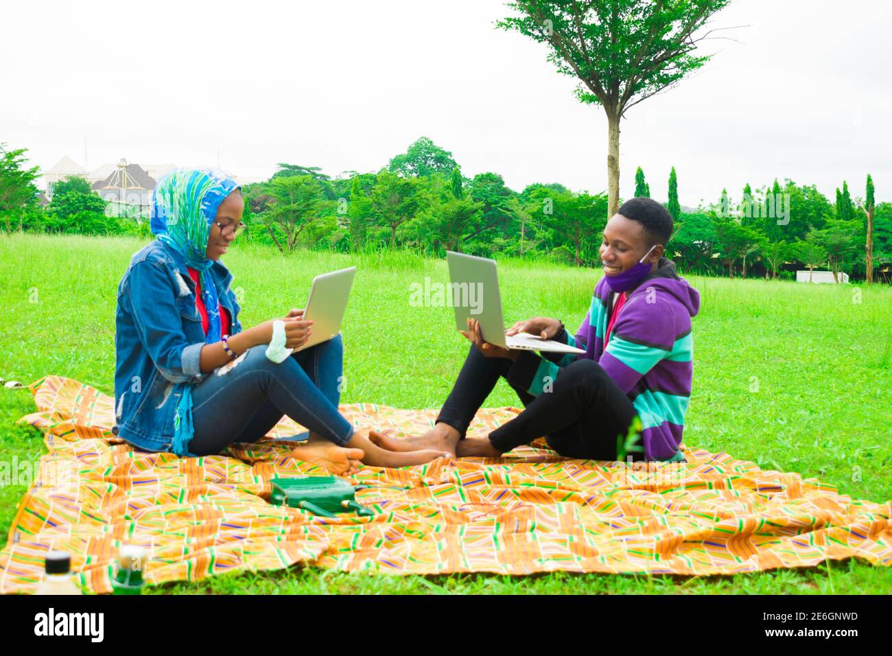 jeunes couples noirs assis dans un parc, utilisant leurs ordinateurs portables pour surfer sur internet Banque D'Images