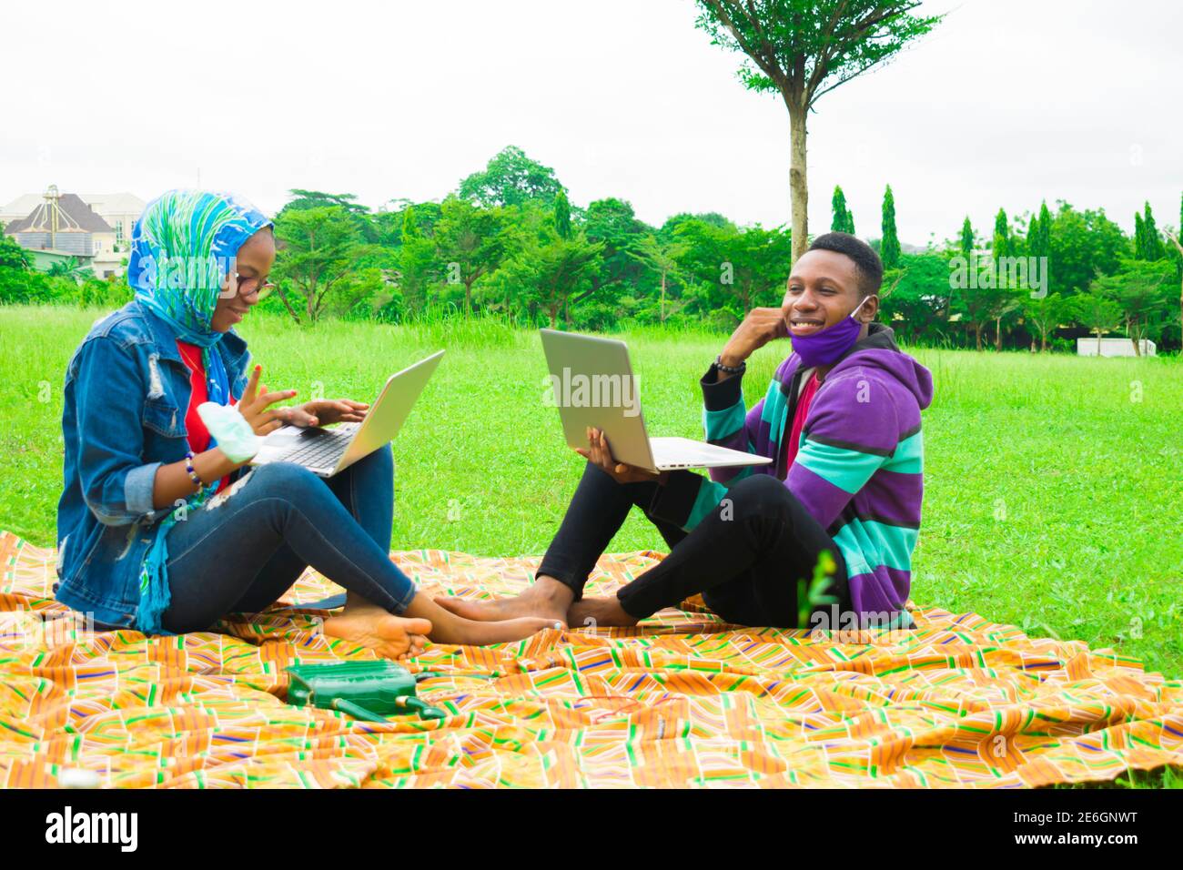 jeunes couples noirs assis dans un parc, utilisant leurs ordinateurs portables pour surfer sur internet Banque D'Images