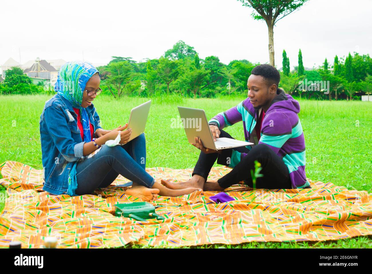 jeunes couples noirs assis dans un parc, utilisant leurs ordinateurs portables pour surfer sur internet Banque D'Images