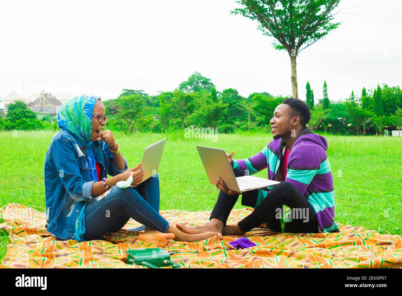 jeunes couples noirs assis dans un parc, utilisant leurs ordinateurs portables pour surfer sur internet Banque D'Images