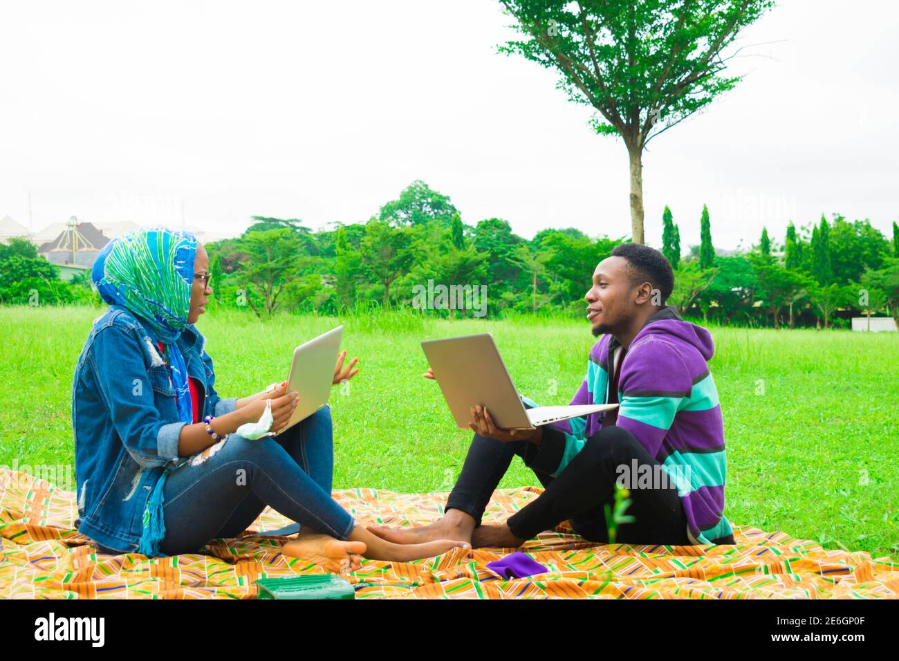 jeunes couples noirs assis dans un parc, utilisant leurs ordinateurs portables pour surfer sur internet Banque D'Images