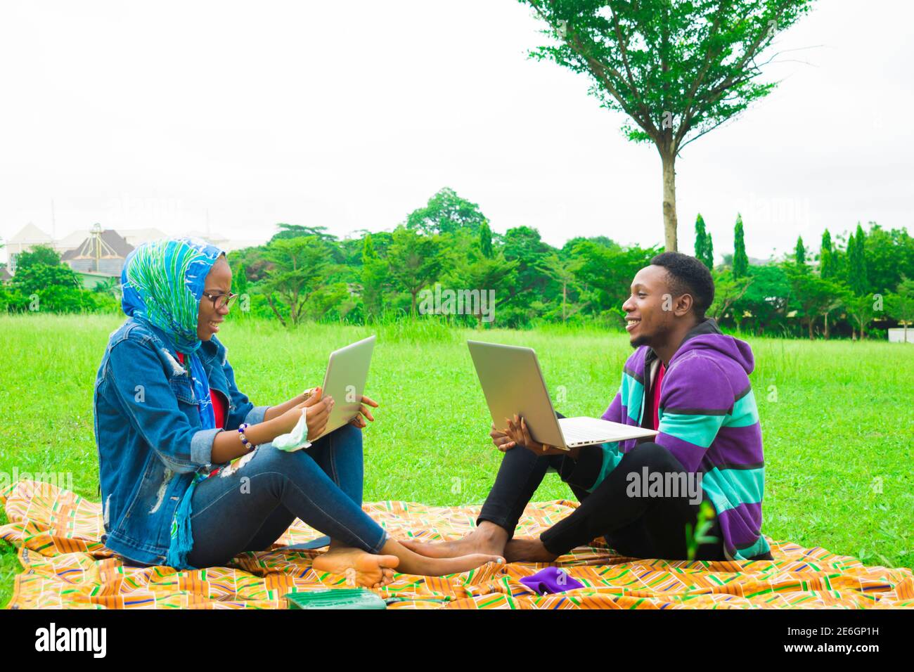 jeunes couples noirs assis dans un parc, utilisant leurs ordinateurs portables pour surfer sur internet Banque D'Images