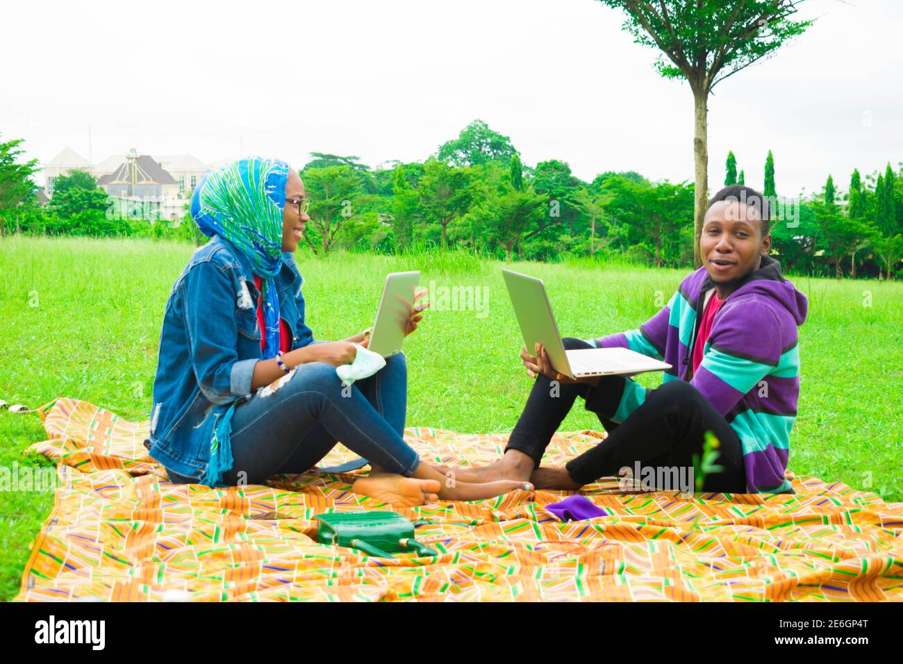 jeunes couples noirs assis dans un parc, utilisant leurs ordinateurs portables pour surfer sur internet Banque D'Images