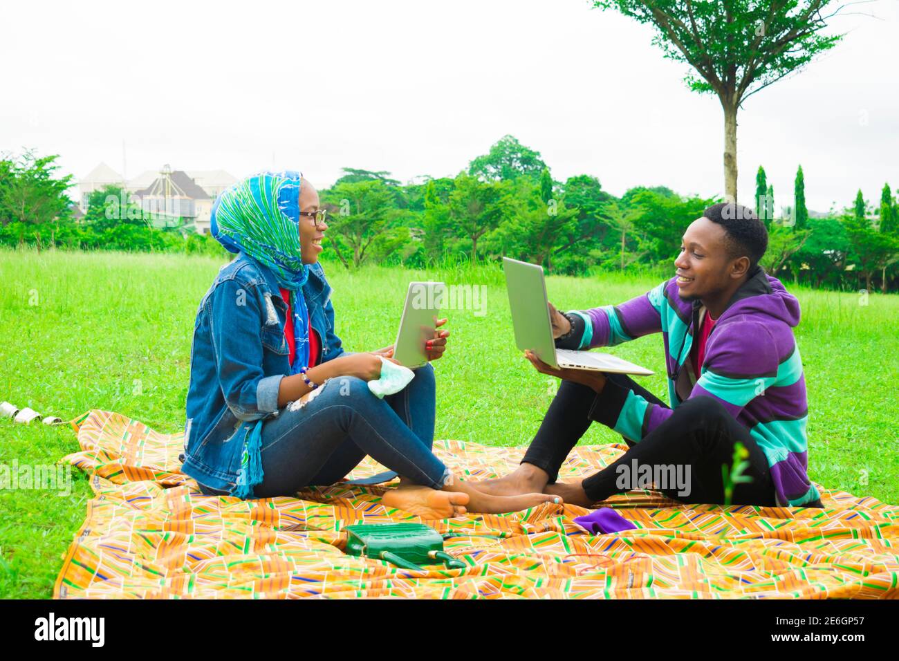 jeunes couples noirs assis dans un parc, utilisant leurs ordinateurs portables pour surfer sur internet Banque D'Images