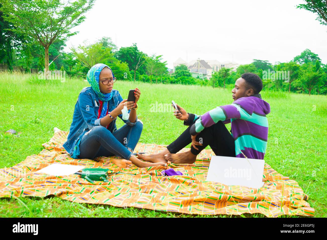jeunes couples noirs assis dans un parc, utilisant leur smartphone pour surfer sur internet Banque D'Images