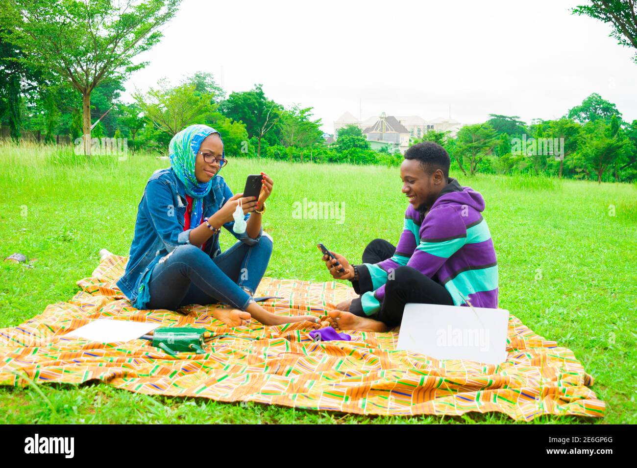 jeunes couples noirs assis dans un parc, utilisant leur smartphone pour surfer sur internet Banque D'Images