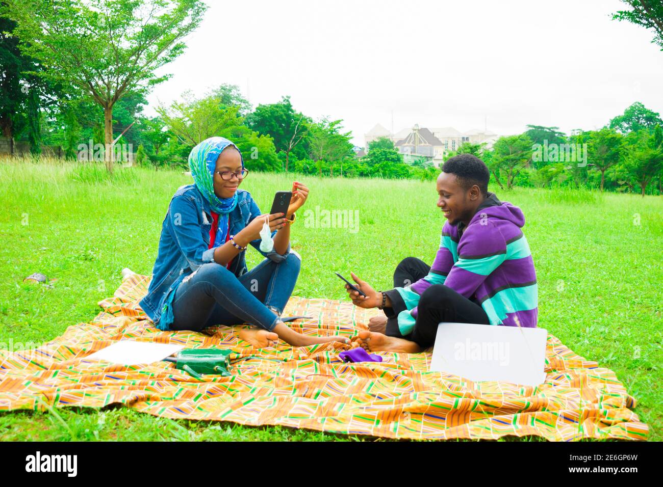jeunes couples noirs assis dans un parc, utilisant leur smartphone pour surfer sur internet Banque D'Images