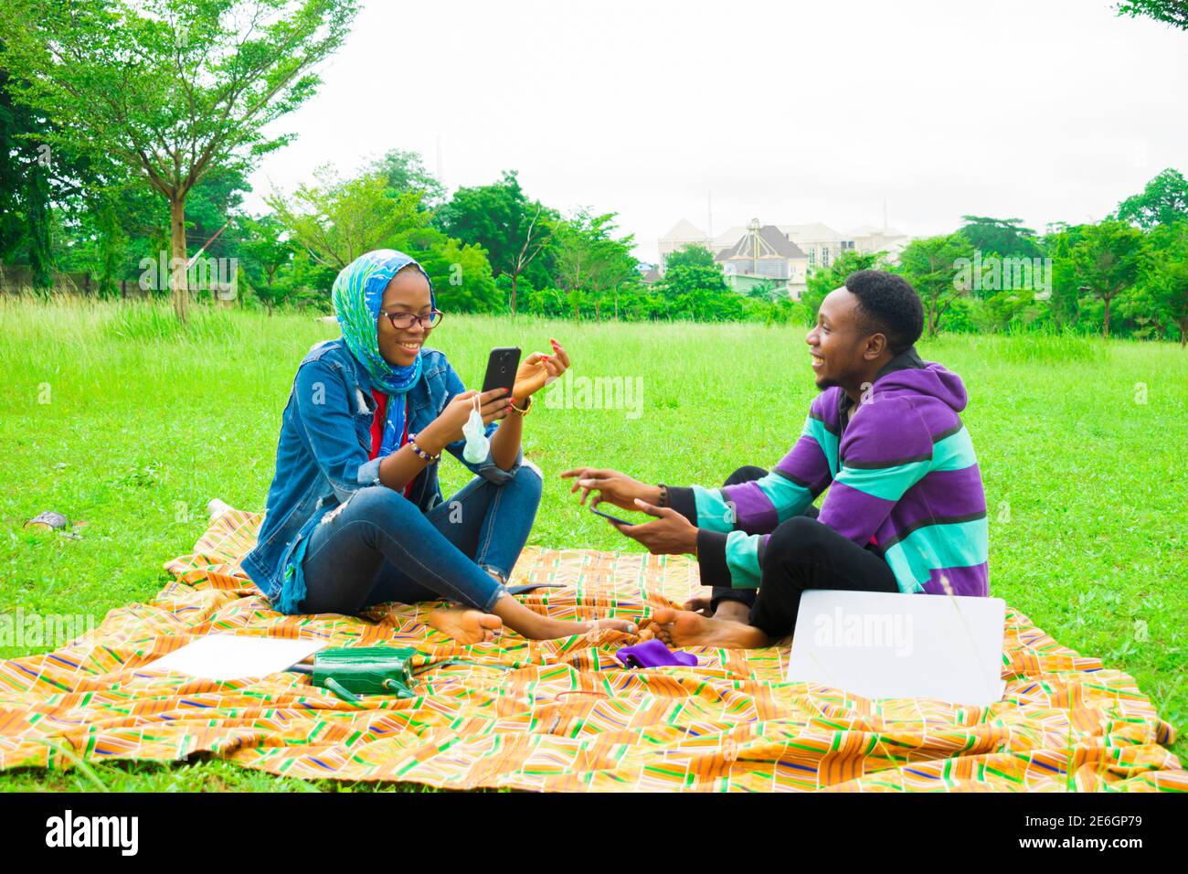 jeunes couples noirs assis dans un parc, utilisant leur smartphone pour surfer sur internet Banque D'Images