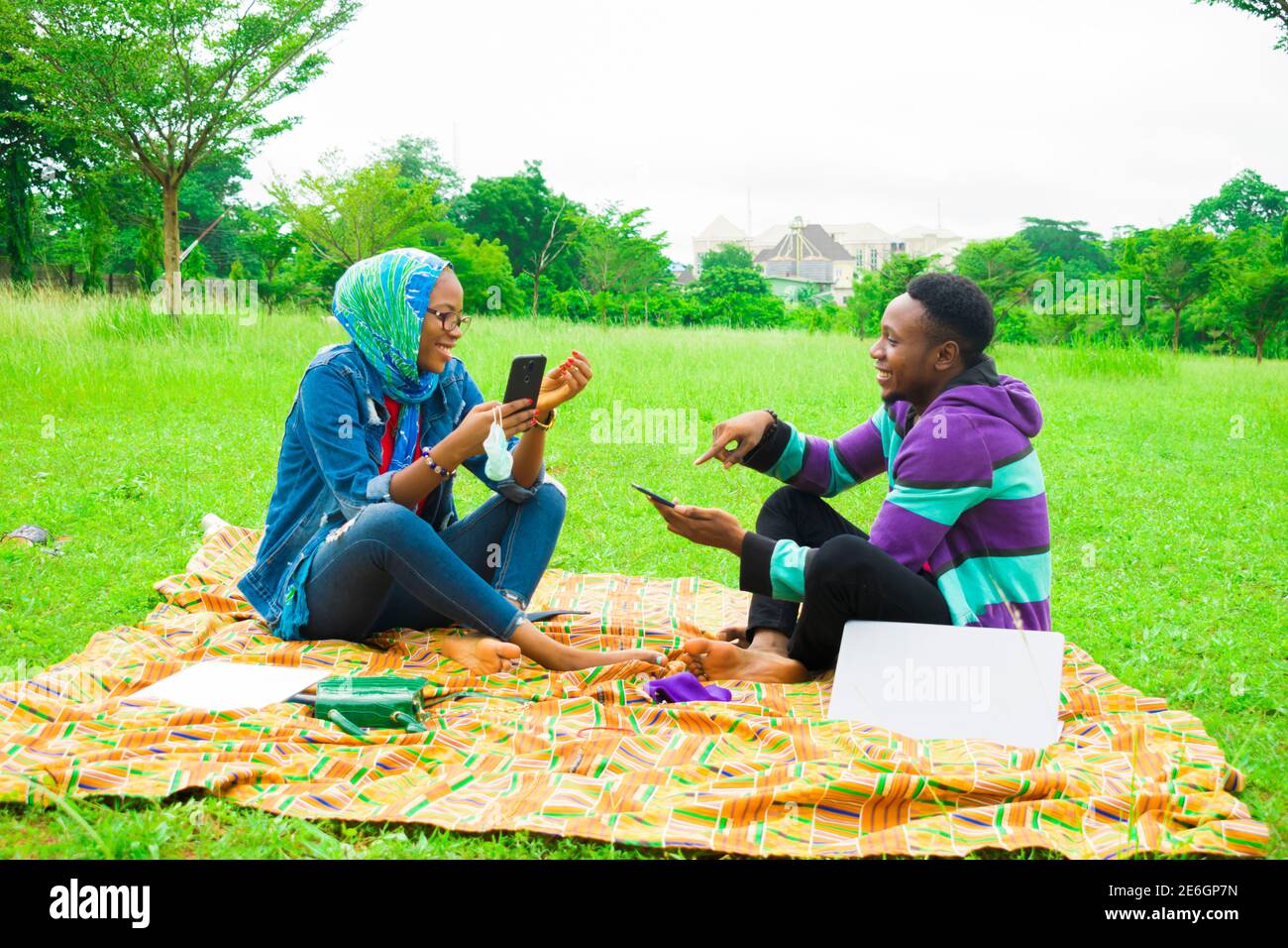 jeunes couples noirs assis dans un parc, utilisant leur smartphone pour surfer sur internet Banque D'Images