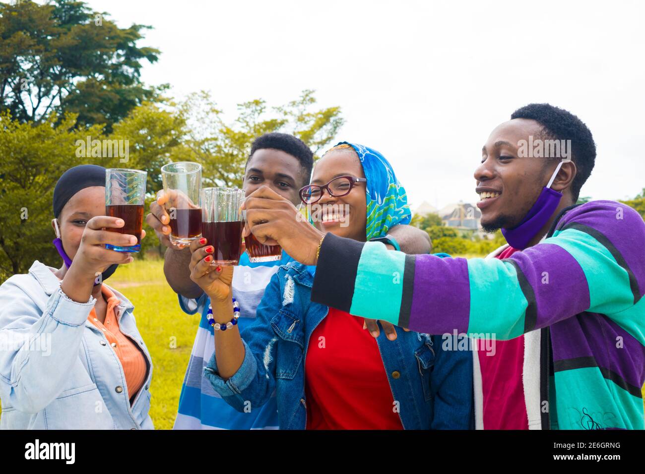 les jeunes gens noirs se tenant dans un parc, donnant un toast avec une boisson dans leurs tasses en verre Banque D'Images