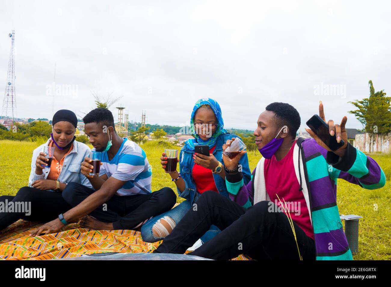 jeunes gens noirs assis dans un parc, buvant de leurs tasses en verre et utilisant un smartphone Banque D'Images