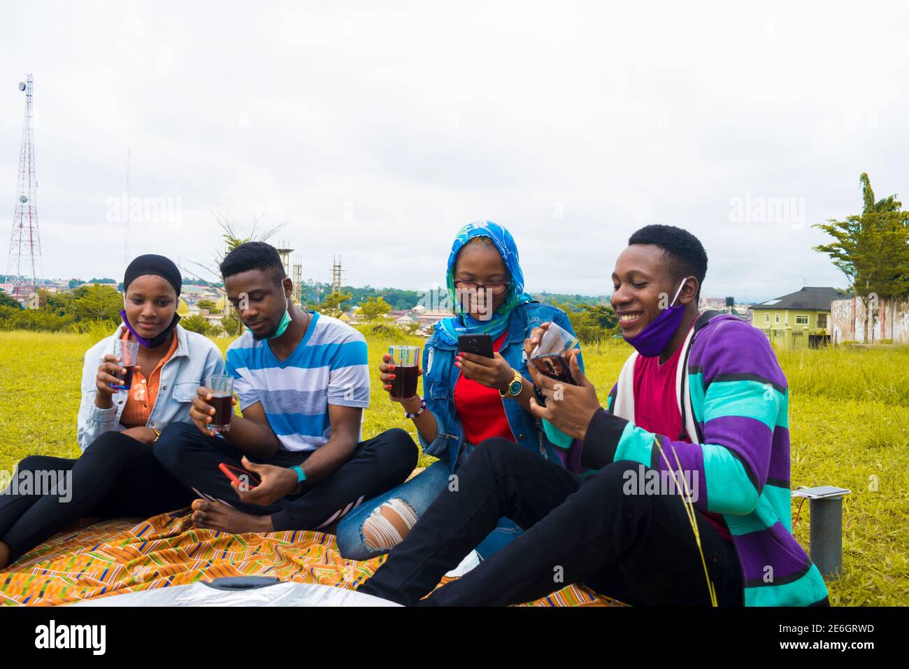 jeunes gens noirs assis dans un parc, buvant de leurs tasses en verre et utilisant un smartphone Banque D'Images