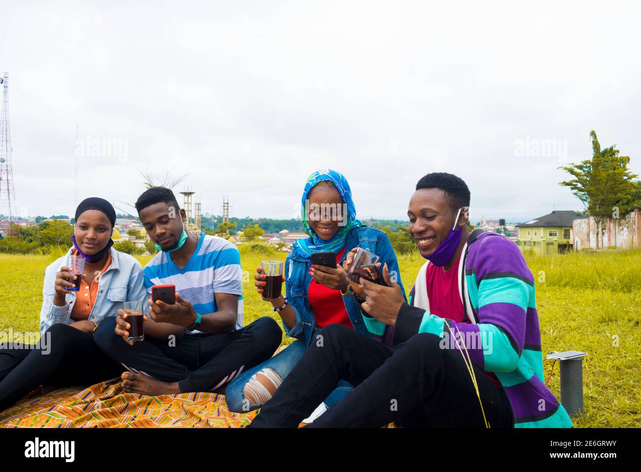 jeunes gens noirs assis dans un parc, buvant de leurs tasses en verre et utilisant un smartphone Banque D'Images