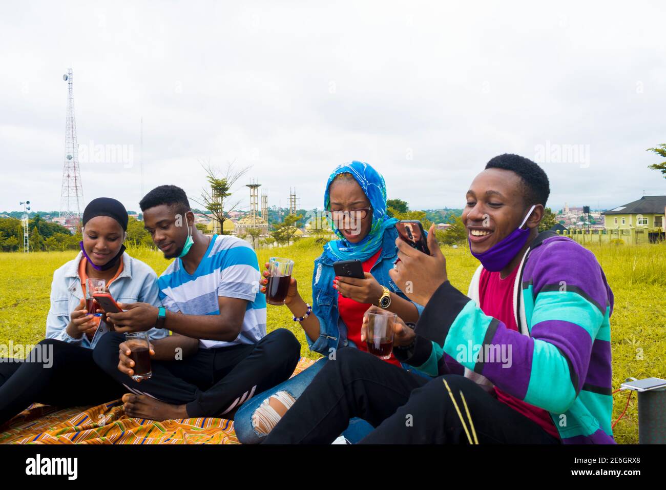 jeunes gens noirs assis dans un parc, buvant de leurs tasses en verre et utilisant un smartphone Banque D'Images