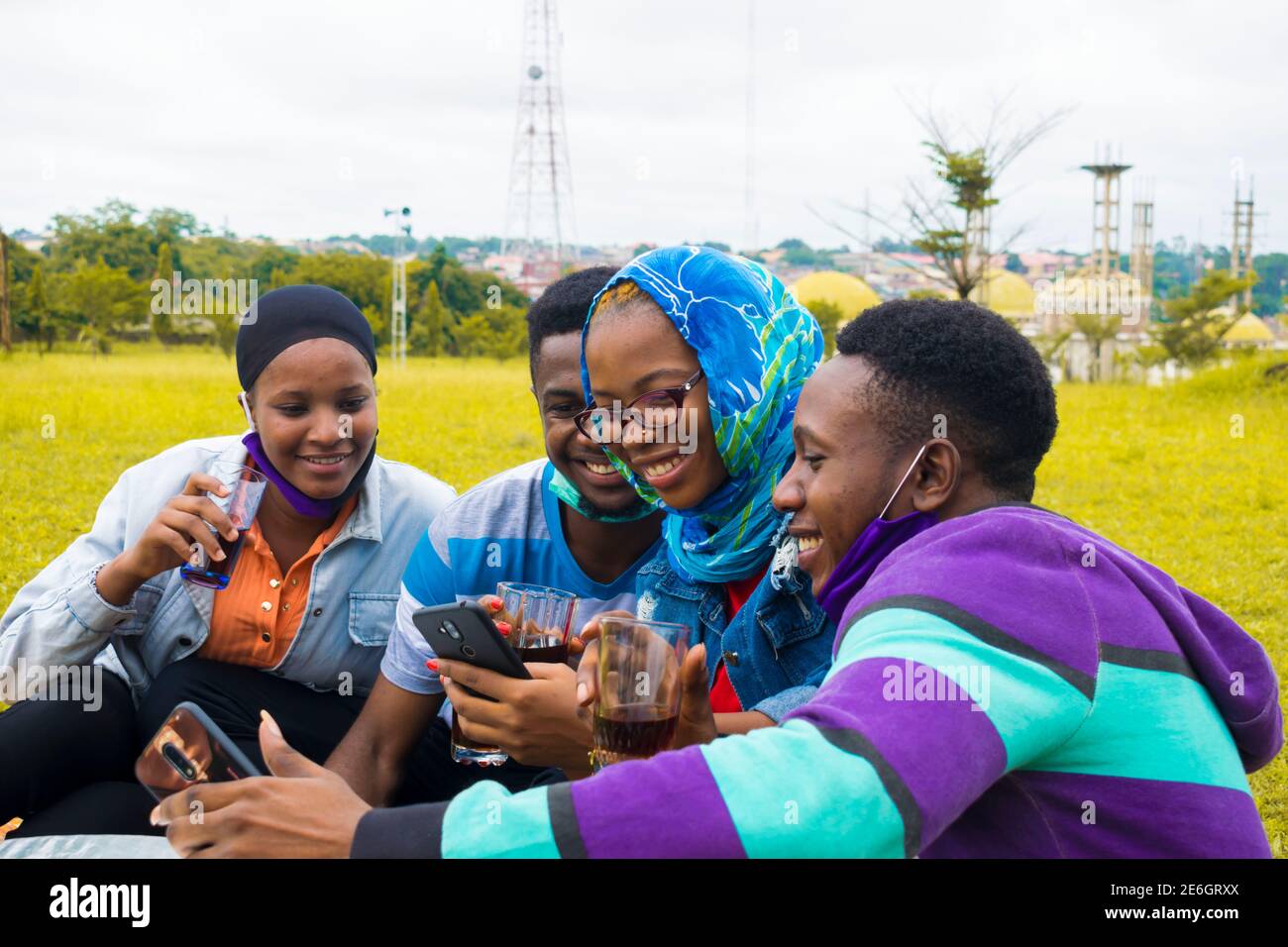 jeunes gens noirs assis dans un parc, buvant de leurs tasses en verre et utilisant un smartphone Banque D'Images