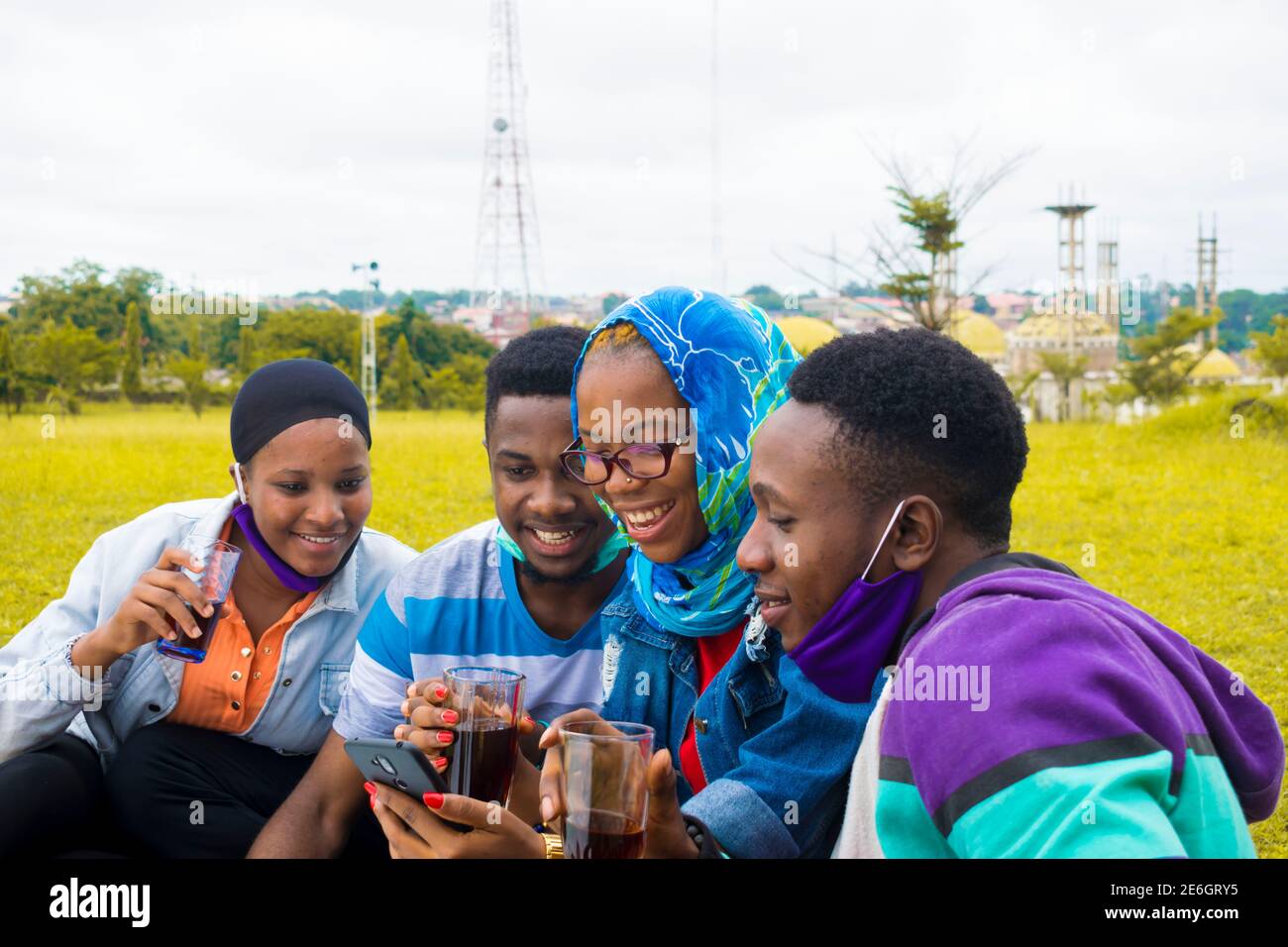 jeunes gens noirs assis dans un parc, buvant de leurs tasses en verre et utilisant un smartphone Banque D'Images