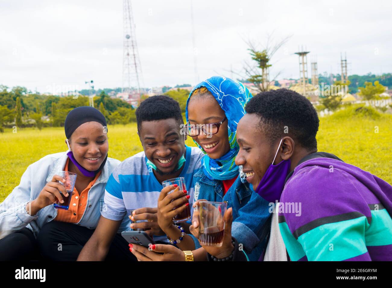 jeunes gens noirs assis dans un parc, buvant de leurs tasses en verre et utilisant un smartphone Banque D'Images