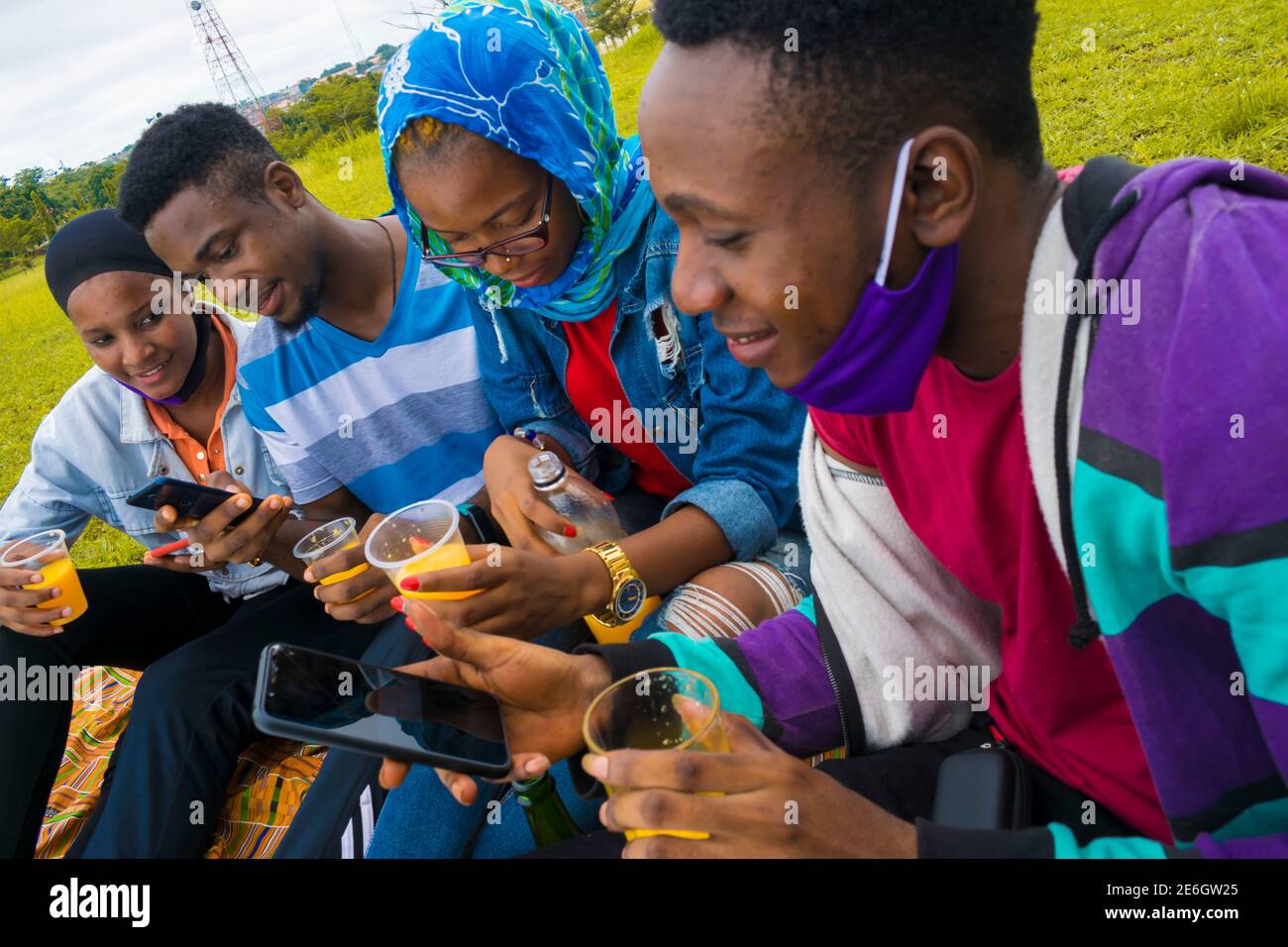 jeunes gens noirs assis dans un parc, buvant de leurs tasses en verre et utilisant un smartphone Banque D'Images