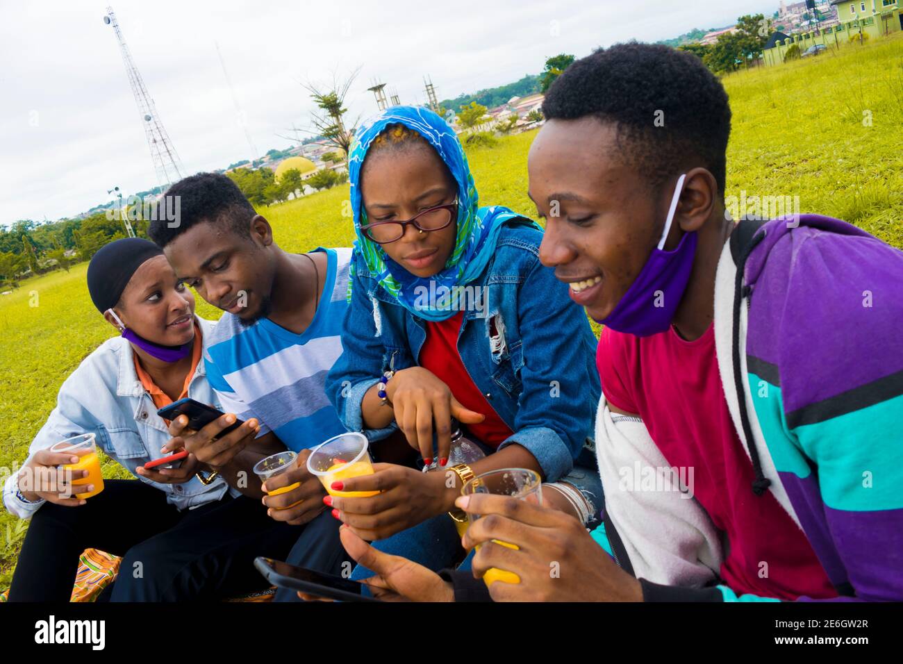 jeunes gens noirs assis dans un parc, buvant de leurs tasses en verre et utilisant un smartphone Banque D'Images