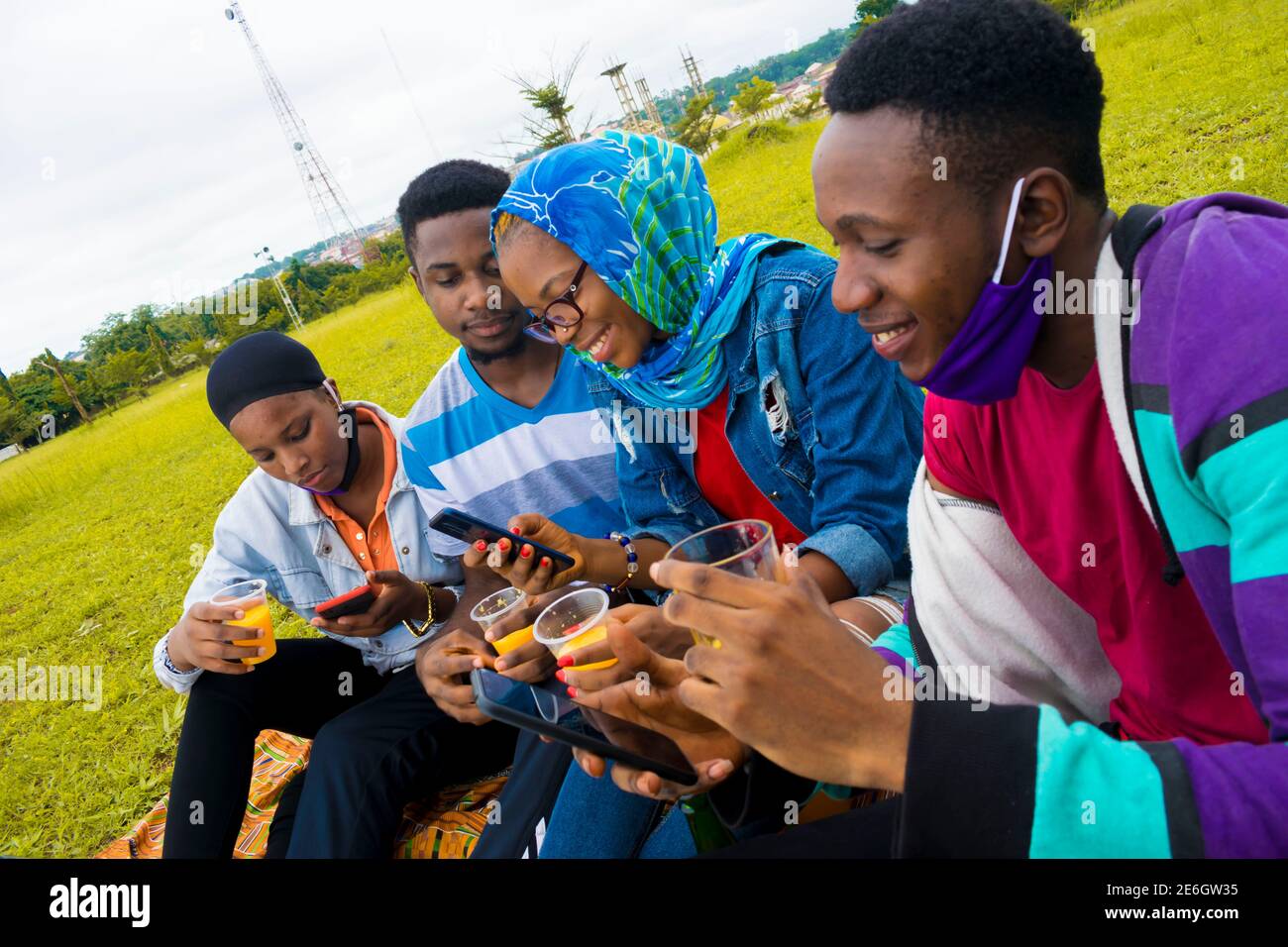jeunes gens noirs assis dans un parc, buvant de leurs tasses en verre et utilisant un smartphone Banque D'Images