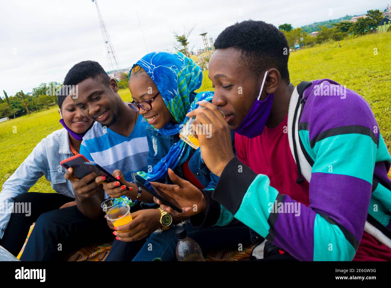 jeunes gens noirs assis dans un parc, buvant de leurs tasses en verre et utilisant un smartphone Banque D'Images