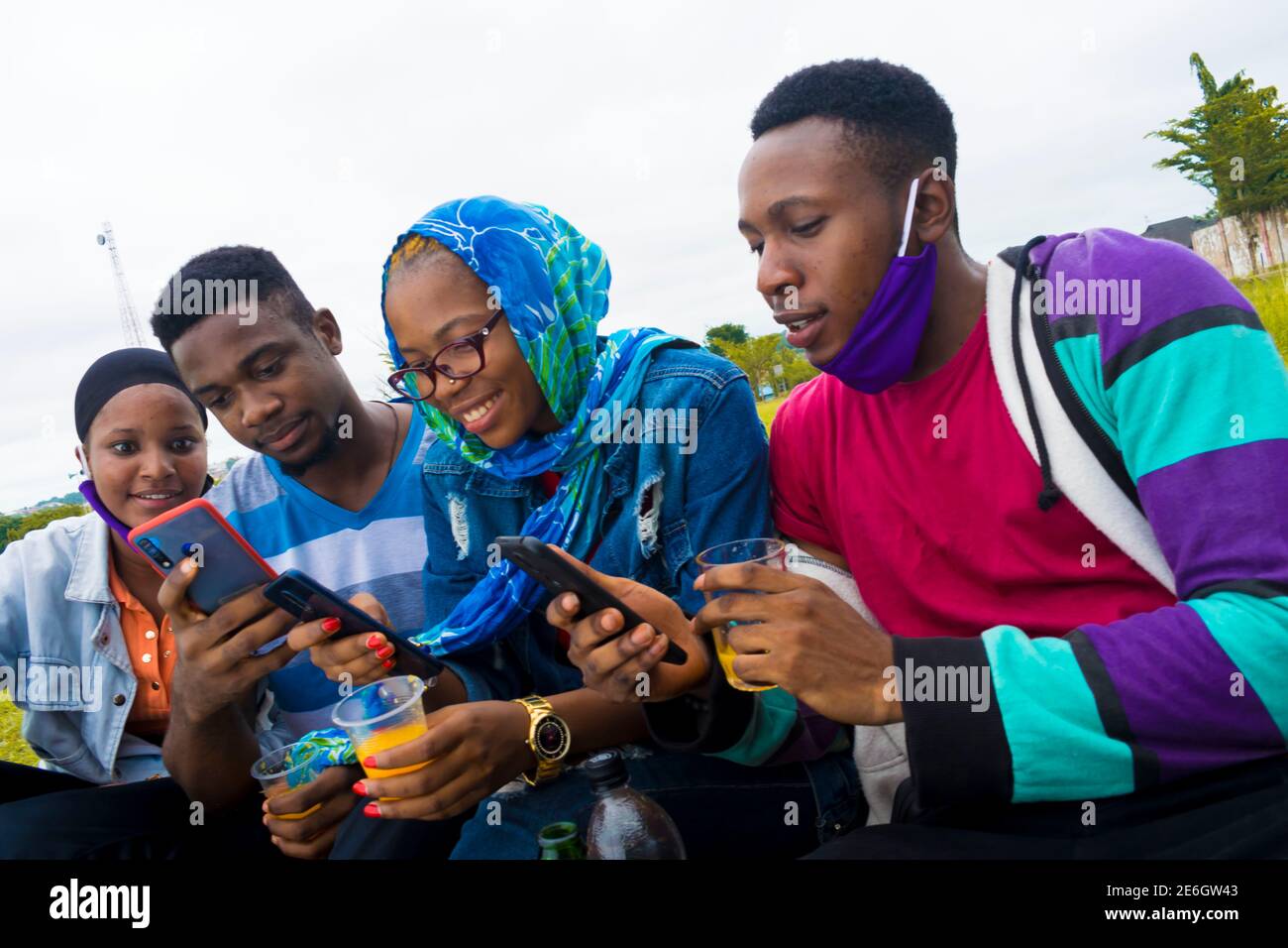 jeunes gens noirs assis dans un parc, buvant de leurs tasses en verre et utilisant un smartphone Banque D'Images