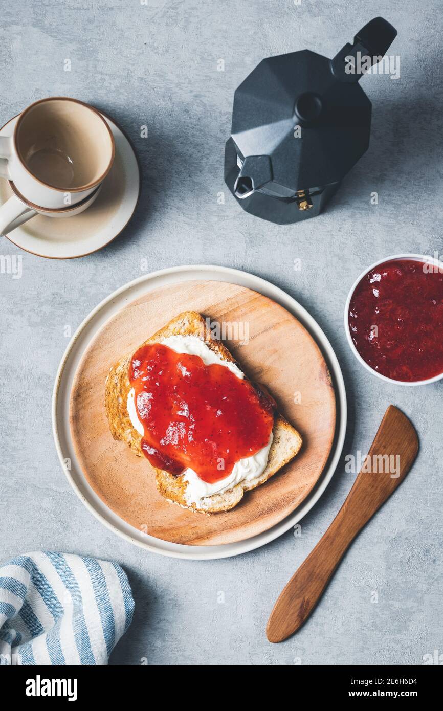 Mise en page de l'ambiance du petit déjeuner avec toasts, fromage à la crème, confiture de fraises et café sur fond texturé gris. Banque D'Images