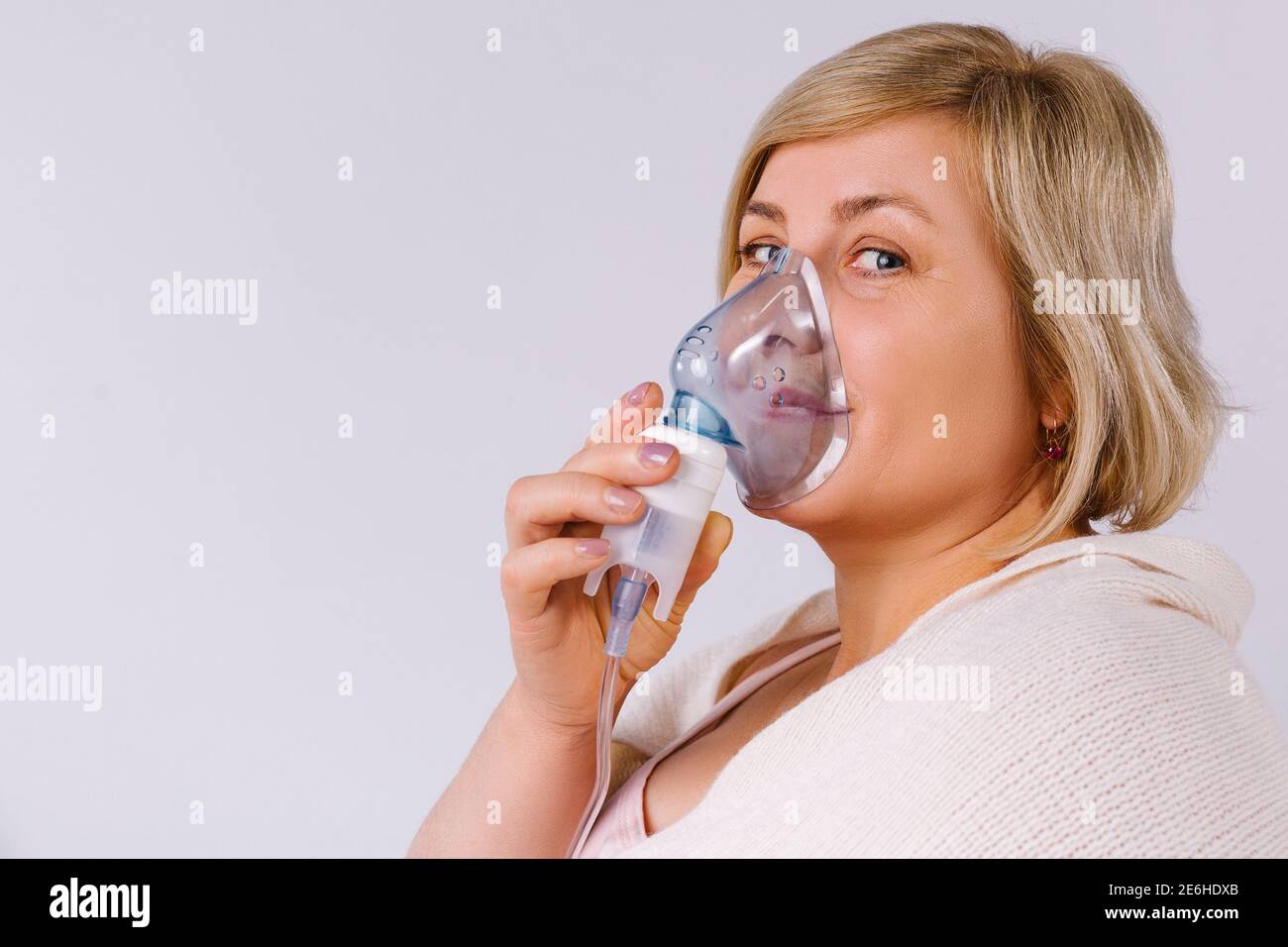 Femme âgée utilisant un nébuliseur fait l'inhalation à la maison et regarde la caméra. Espace vide pour la publicité. Banque D'Images