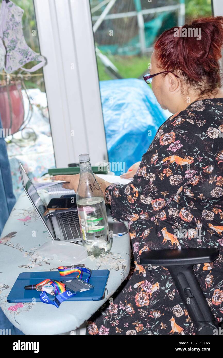 Femme noire travaillant à la maison (WFH) utilisant une planche à repasser pour un bureau dans un cadre domestique. Banque D'Images