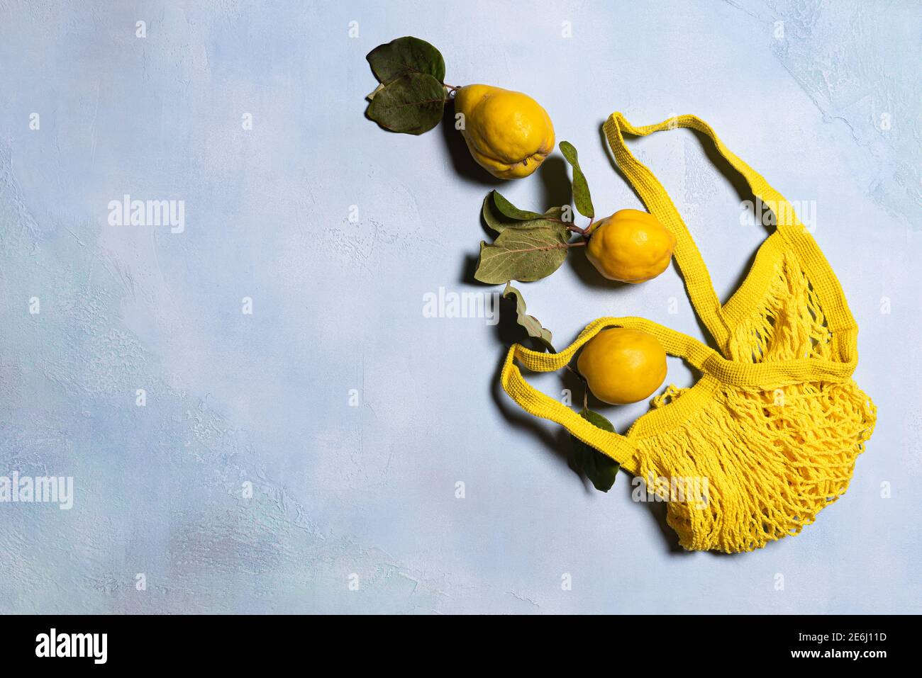 Trois pommes de coing et un sac en maille jaune sur fond bleu. Directement au-dessus de la vue. Les fruits et les feuilles ont des imperfections naturelles, des taches et des rayures. Ha Banque D'Images